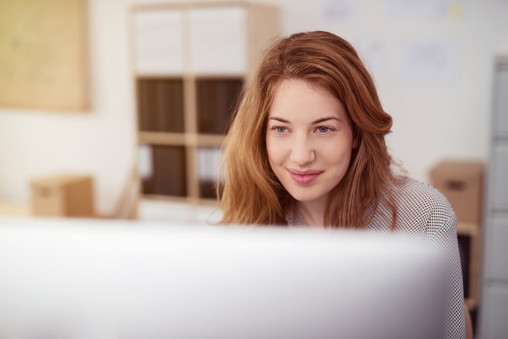 Attractive young woman working on a desktop computer smiling as she leans forwards reading text on the screen, view over the monitor-Apr-24-2024-11-55-43-8011-AM