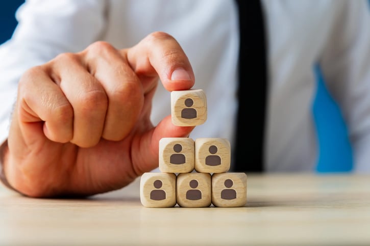 Ejecutivo de negocios apilando dados de madera con íconos de personas en forma de pirámide, simbolizando estructura organizacional, jerarquía u organigrama