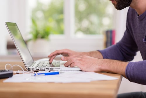 Close up low angle view of a man working from home on a laptop computer sitting at a desk surfing the internet-2