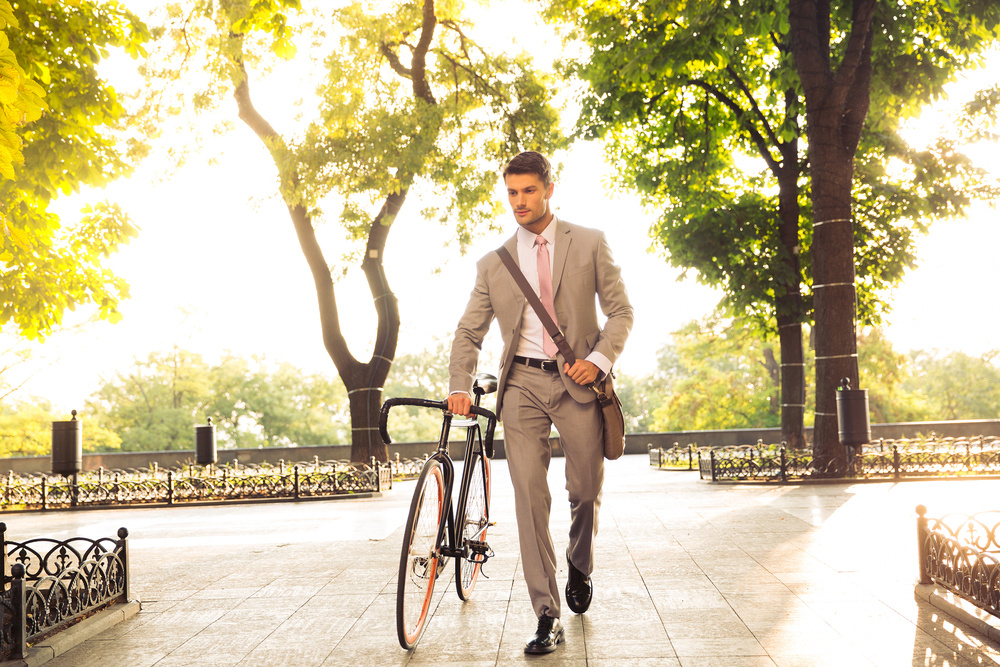 Joven empresario seguro de sí mismo paseando con su bicicleta por la calle en la ciudad