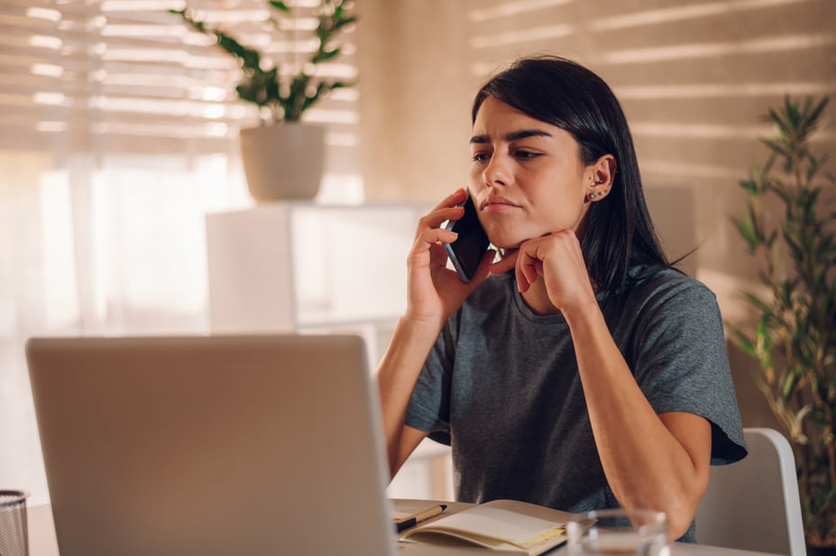 Frustrated employee calling in sick after a denied vacation request, sitting at home with a phone in hand.