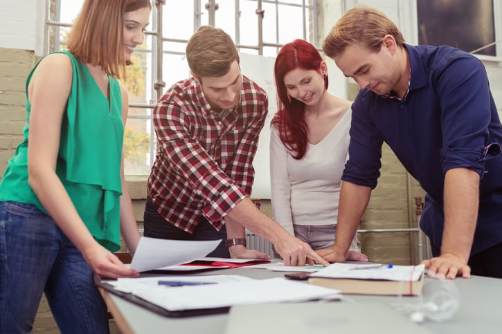 Group of Young colleagues Discussing the Project Paper at the Table While in Standing Position