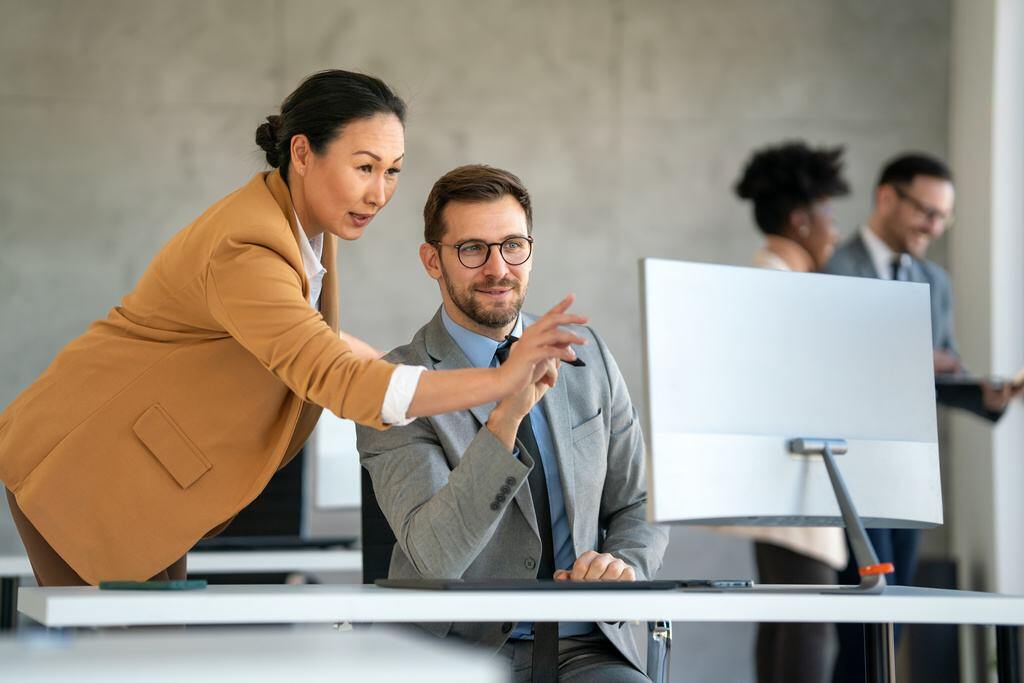 Manager showing explaining process to new employee on computer screen