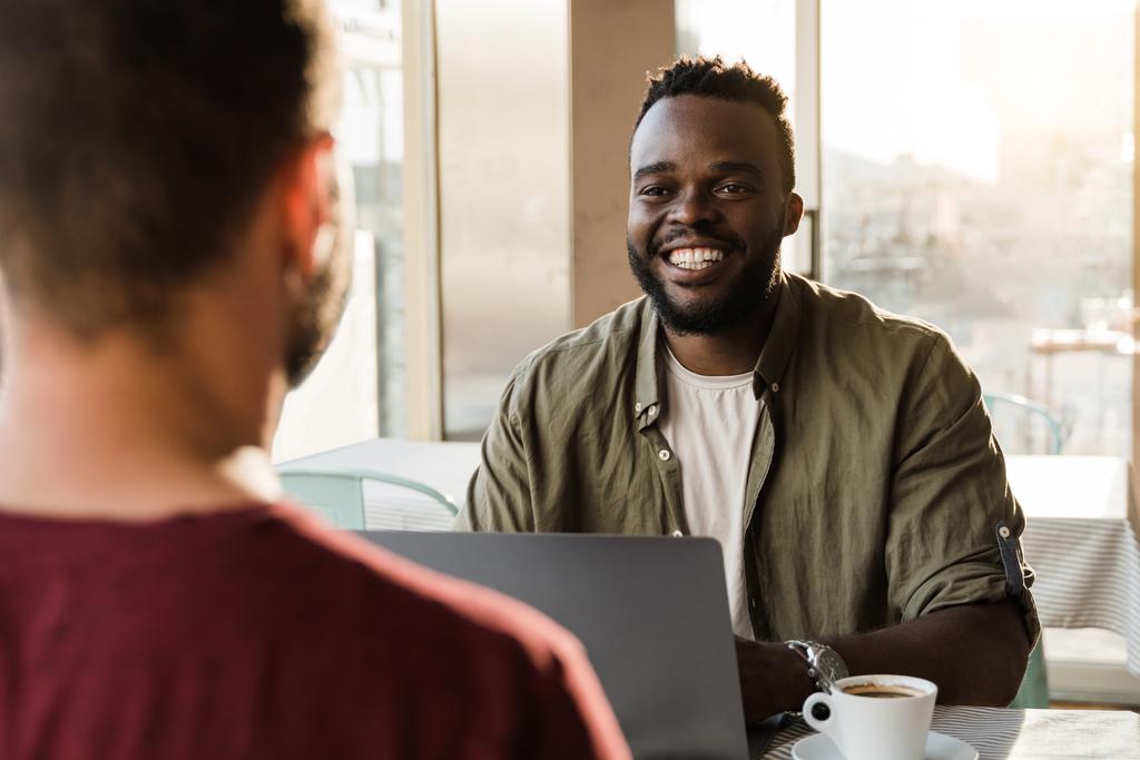 Multiracial people having a chat or interview and using laptop indoor at bar restaurant - Focus on african man