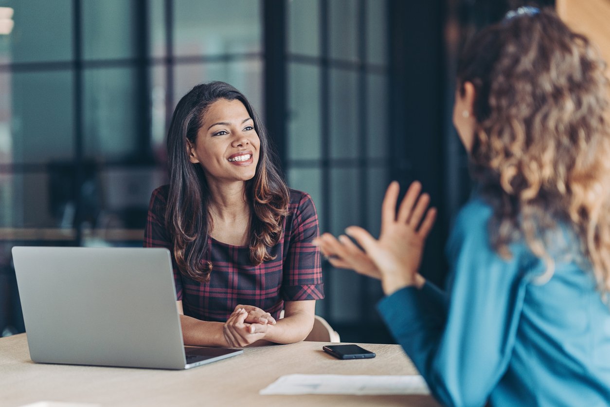 Smiling female hiring manager with her laptop listening to female applicant in blue shirt during an interview inside an office