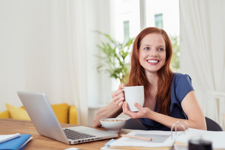 Mujer Joven Pensativa Desayunando en su Despacho, Mostrando una Expresión Facial Feliz.