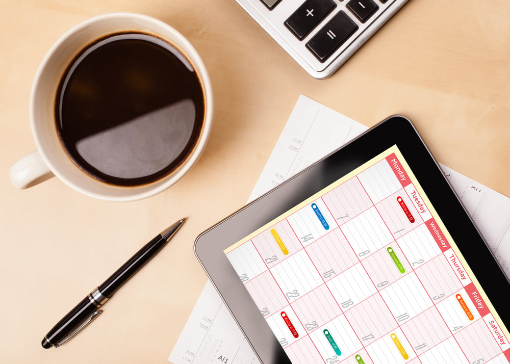 Workplace with tablet pc showing calendar and a cup of coffee on a wooden work table close-up-Jun-16-2023-07-39-52-0101-AM