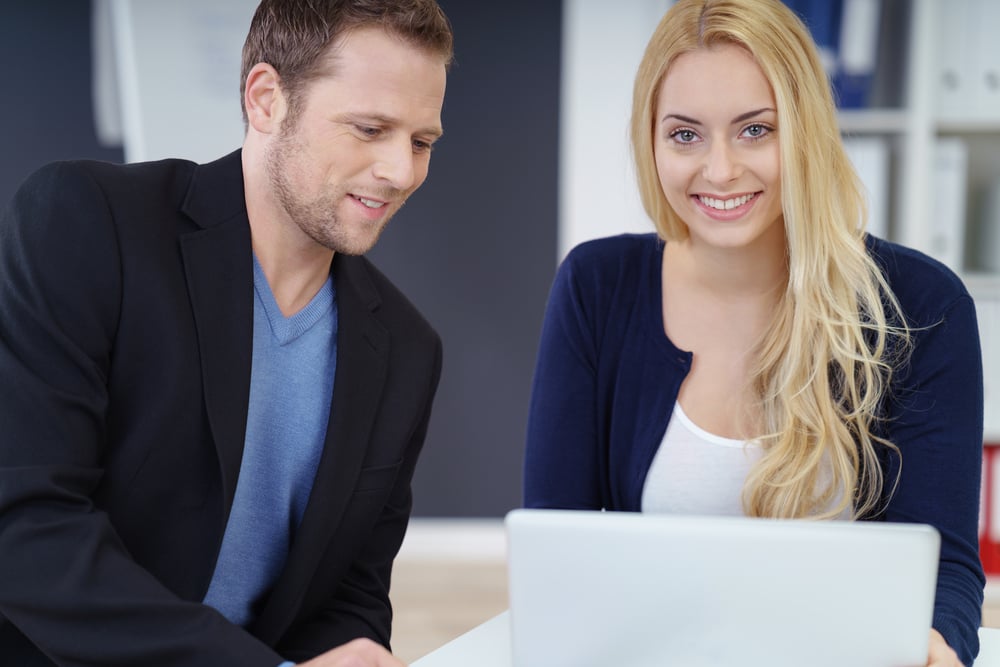 Young business colleagues working as a team sitting together at a desk sharing a laptop computer with focus to a smiling friendly woman