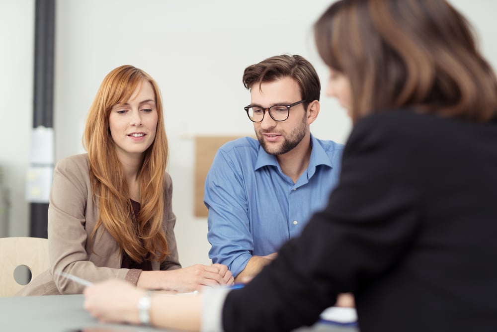 Broker making a presentation to a young couple showing them a document which they are viewing with serious expressions