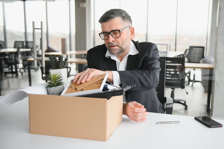 Empleado despedido guardando sus pertenencias en una caja debido a jubilación anticipada involuntaria