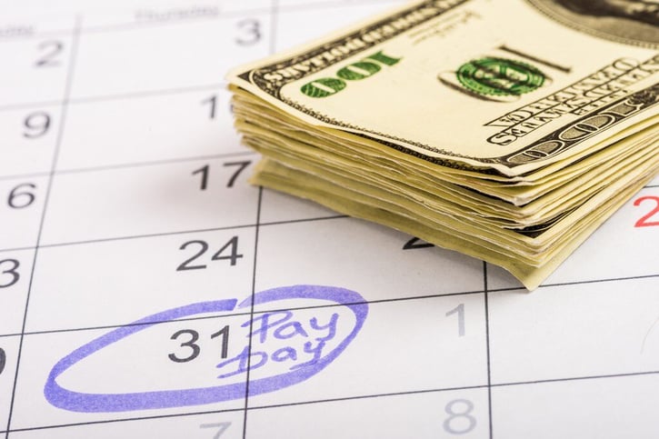 selective focus on calendar circling pay day with dollars/money on top symbolising biweekly pay