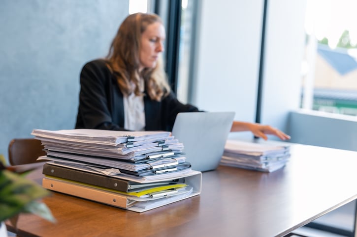 Mujer trabajando con una pila de documentos sobre una mesa que simboliza el sobrecarga de trabajo