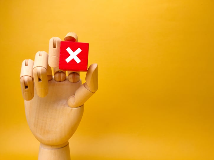 wooden hand holding block with error sign symbolising blacklisting in the workplace